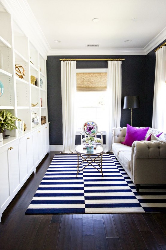 a small living room with black walls and a large white storage unit, a neutral upholstered sofa, a striped black and white rug for a contrasting look
