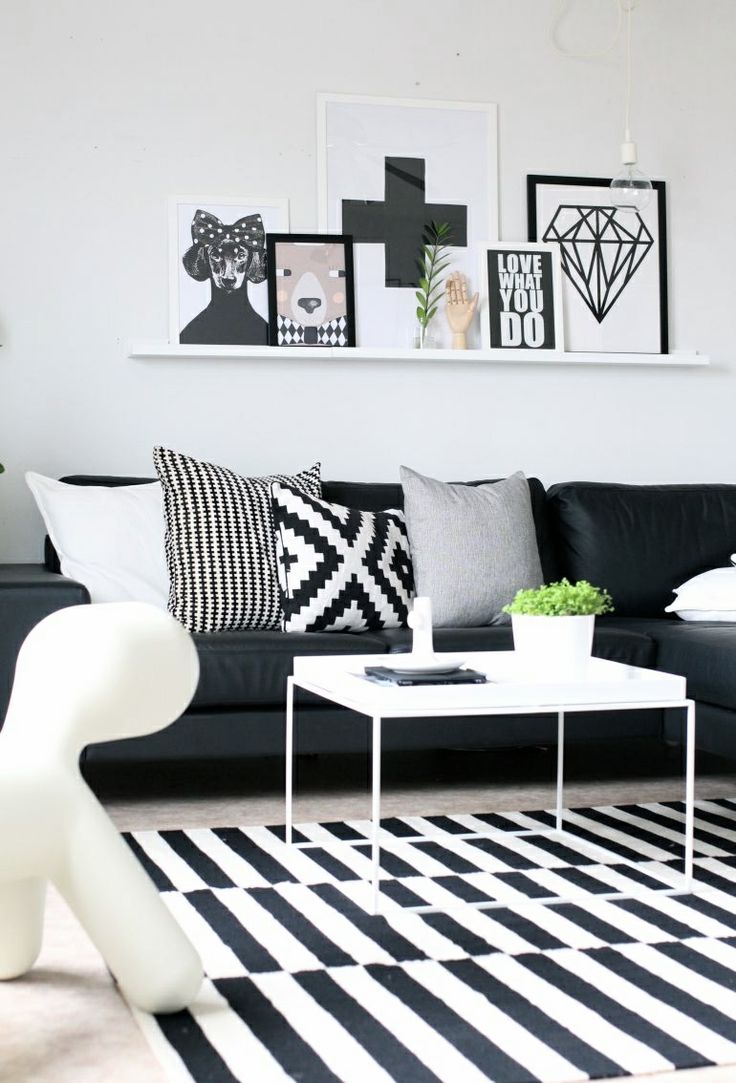 a black and white Scandinavian living room with a black sofa and printed pillows, a striped rug and a gallery wall on a ledge