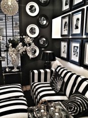 a refined vintage-inspired black and white living room with black walls, a black and white strip sofa and poufs, a black and white gallery wall and some decorative plates
