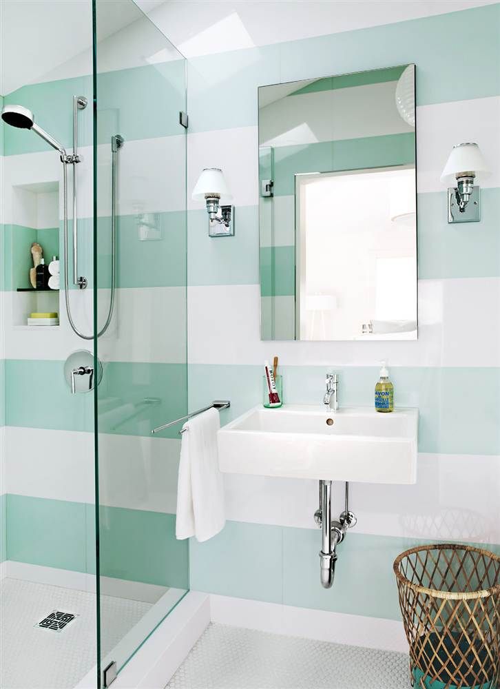 a contemporary bathroom with mint and white striped walls, a small shower space and a wall mounted sink, a mirror and a basket