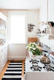 a small neutral kitchen with white cabinets, open shelving is given eye-catchiness with a black and white striped rug