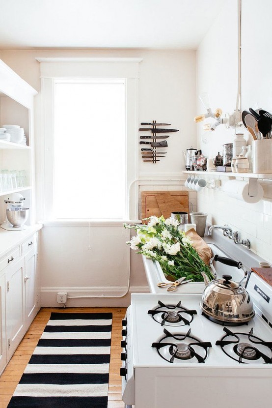 a small neutral kitchen with white cabinets, open shelving is given eye-catchiness with a black and white striped rug