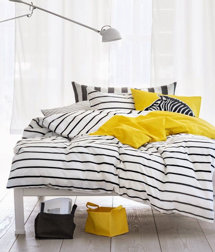 a bed with black and white bedding is accented with some yellow pillows and a blanket looks very fresh and bold