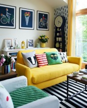 a fun and colorful living room with tan walls, a yellow sofa with bold pillows, a neutral chair, a bold stripe rug, an accent wall wiht a grandfather’s clock and a gallery wall