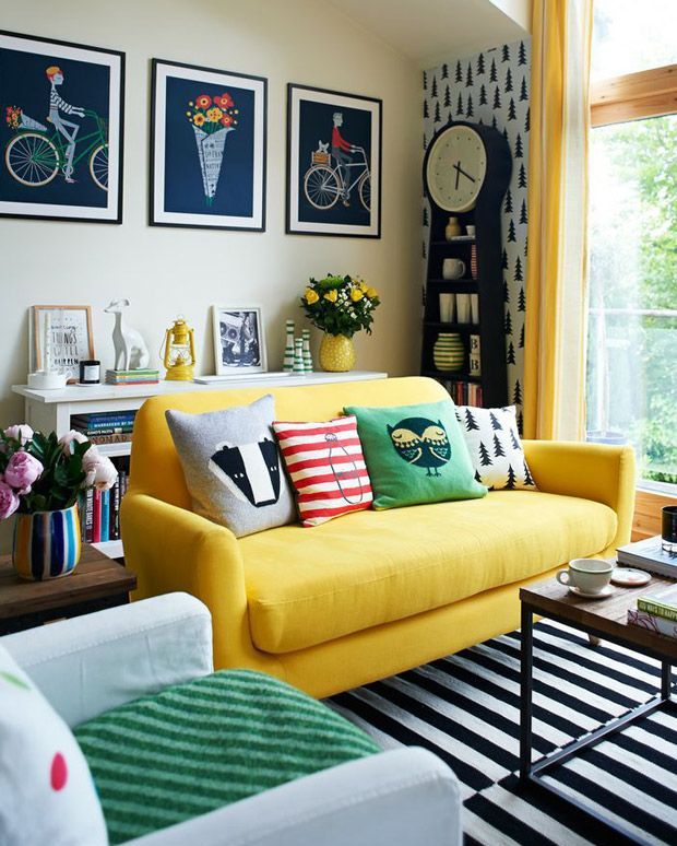 a fun and colorful living room with tan walls, a yellow sofa with bold pillows, a neutral chair, a bold stripe rug, an accent wall wiht a grandfather's clock and a gallery wall