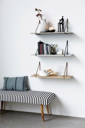 a black and white strip upholstered bench with pillows and some hanging shelves over it is a a cool and welcoming space