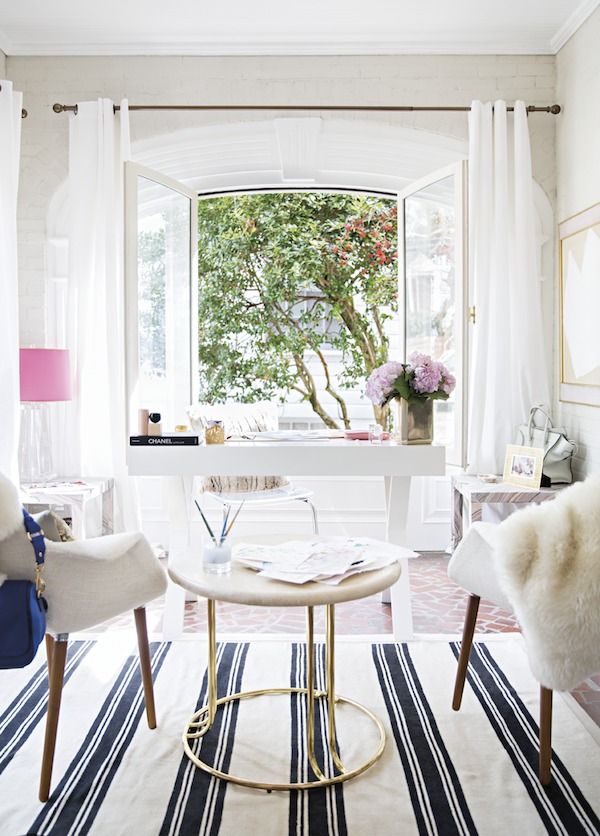 a neutral home office wiht a chic white desk, white chairs and a coffee table, pink touches and a cool view of the garden