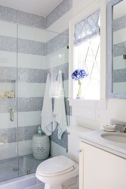 a delicate bathroom with grey and white strip walls, a shower space and some white furniture welcomes in and looks nice