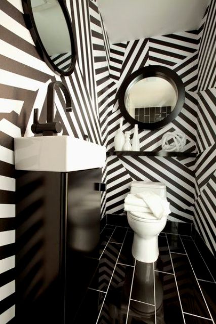 a black and white powder room done with stripe wallpaper walls, a black vanity, mirrors in black frames