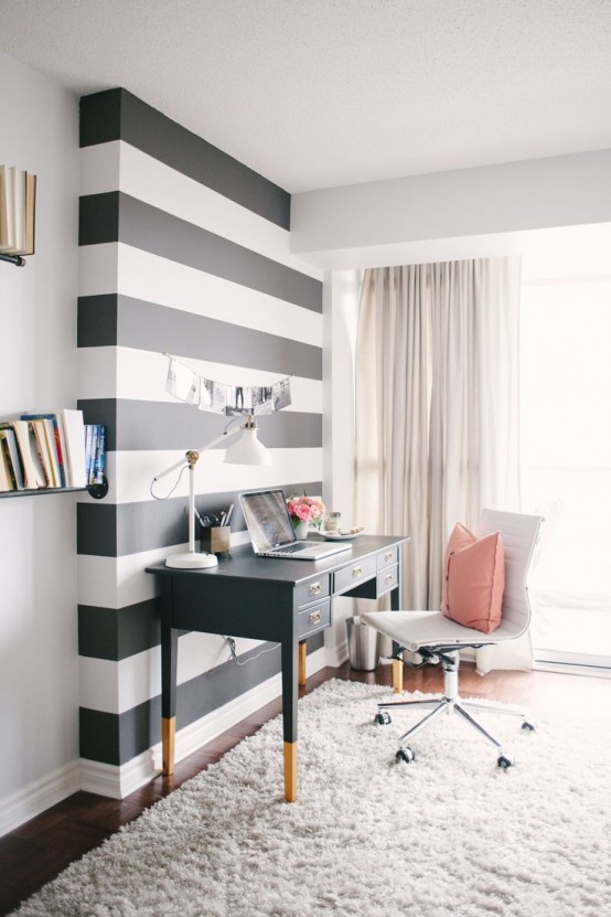 a cozy home office nook with a black and white accent wall, a refined black desk and a neutral chair plus a pink pillow is cute and welcoming