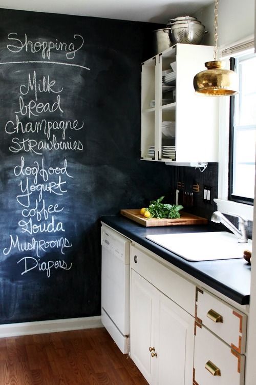 a welcoming farmhouse kitchen with neutral cabinets, a chalkboard accent wall, pendant lamps and black stone countertops