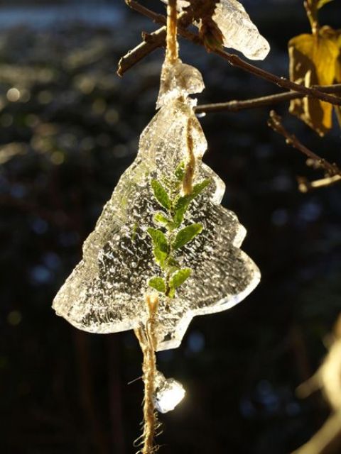an ice Christmas tree-shaped ornament with some leaves inside and some threads to hang it is a cool rustic decor idea for a winter garden
