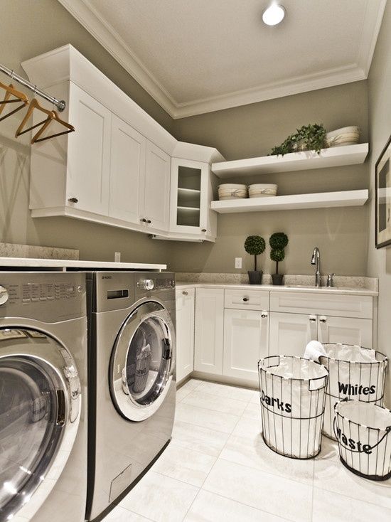 a modern farmhouse laundry with grey walls, white shaker style cabinets, open shelves, a washing machine and a dryer, a holder for clothes hangers and potted greenery