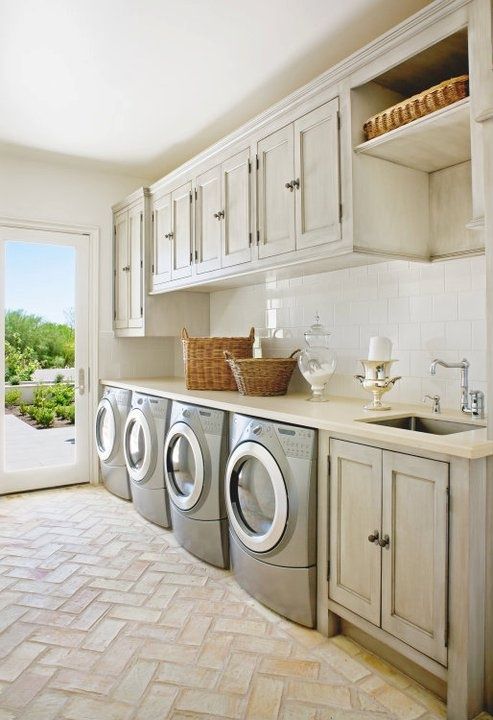 a stylish creamy laundry with shaker style cabinets, a large console table over the washing machines and driers, a vanity with a sink