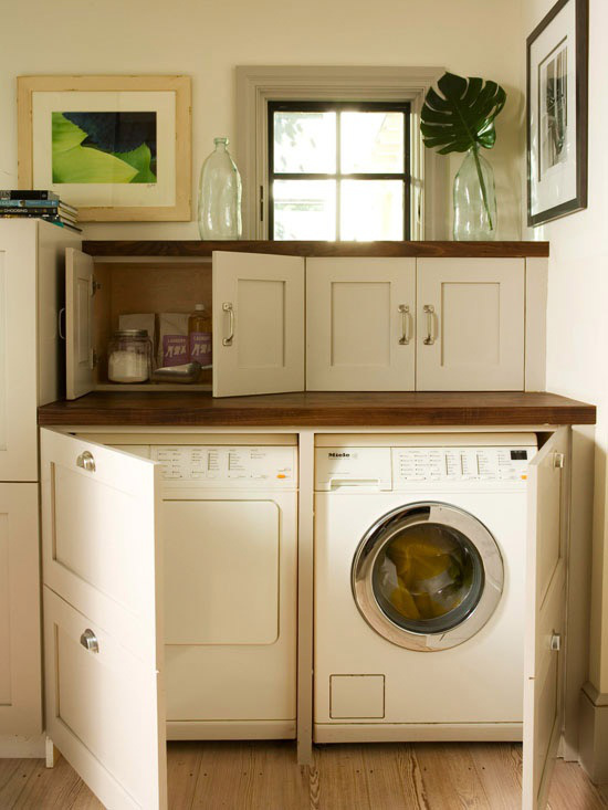 a white farmhouse laundry with shaker style cabinets, dark stained countertops, colorful artwork and greenery in a jar