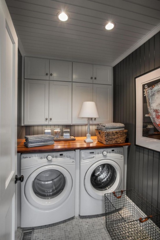 a small farmhouse with black planked walls, white shaker style cabinets and a washing machine and dryer and a stained countertop and a basket