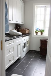 a neutral farmhouse laundry space with shaker style cabinets, black coutnertops and black tiles, baskets for storage and potted plants is a lovely space to be in