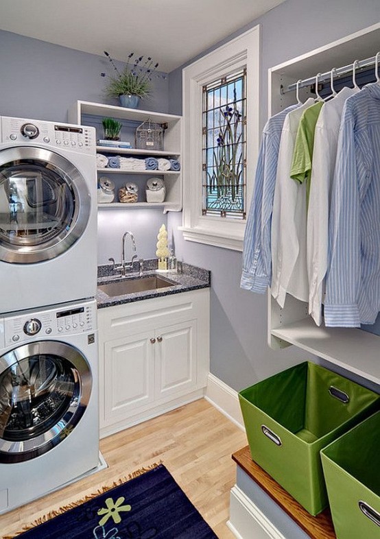 a cute country style laundry with lilac walls, white shaker style cabinets with black countertops, an open storage unit, green baskets and a stacked washing machine and a dryer