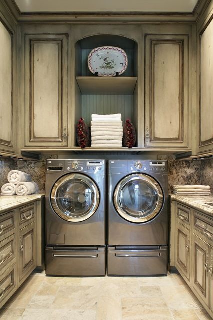 a neutral vintage laundry with lovely shaker style cabinets, open shelves, stone countertops and stone tiles plus a stainless steel washing machine and dryer