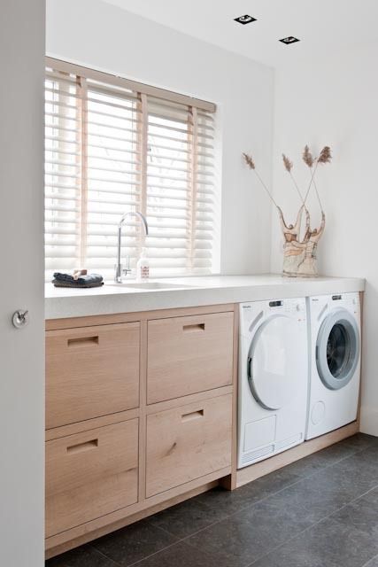 a neutral laundry with sleek light-stained drawers, a concrete countertop, a washing machine and dryer and some grasses