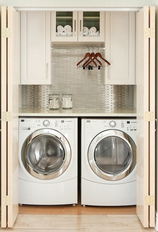 a white laundry with shaker style cabinets, silver tiles on the wall, a washing machine and a dryer and a countertop and clothes hangers
