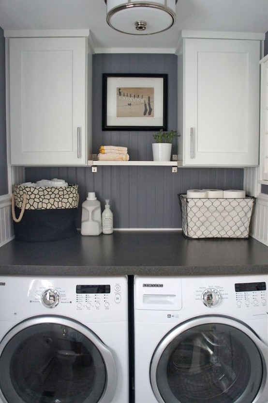 a modern farmhouse laundry with shaker style cabinets, a graphite grey wall, a black countertop and a washing machine and a dryer