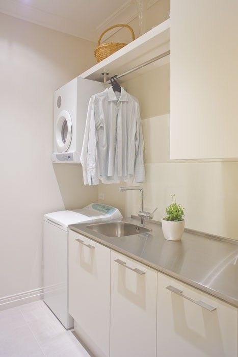 a clean neutral laundry with sleek cabinets, a metal countertop, some clothes hangers and a sink, plus a washing machine