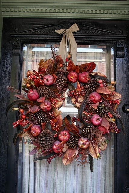 a moody fall wreath of pinecones, faux berries, pomegranates, grasses, foliage and feathers for a boho feel