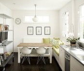 a small contemporary kitchen in white, with an L-shaped bench, a wooden top table, a large open storage unit