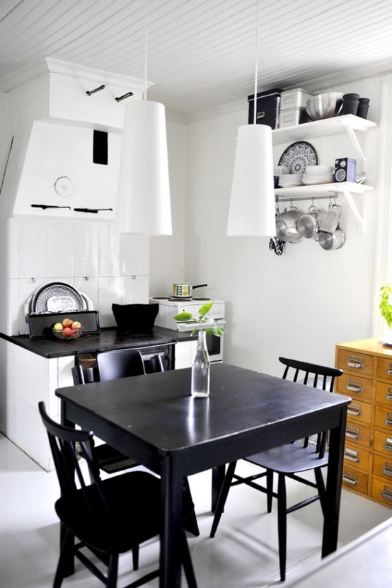 a small eclectic kitchen with a white cabinet, a black countertop, white pendant lamps, a vintage black dining set and an apothecary cabinet