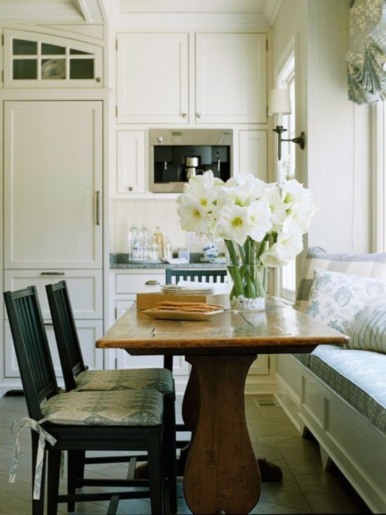 a small neutral farmhouse kitchen with grey countertops, a wooden table, black chairs and an upholstered blue bench