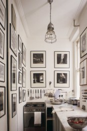 a small monochromatic kitchen done with neutral cabinets and countertops, black and white photos on the walls and a pendant lamp