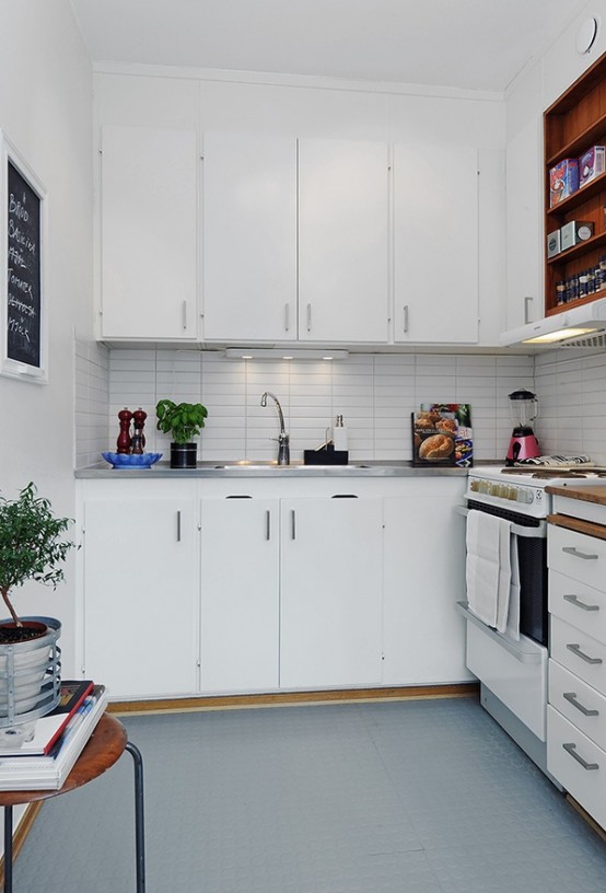 a small minimalist kitchen in white, with a tile backsplash, lights and a stool for storage