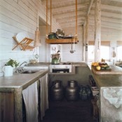 a small rustic meets industrial kitchen with concrete countertops, metal churns and suspended wooden shelves