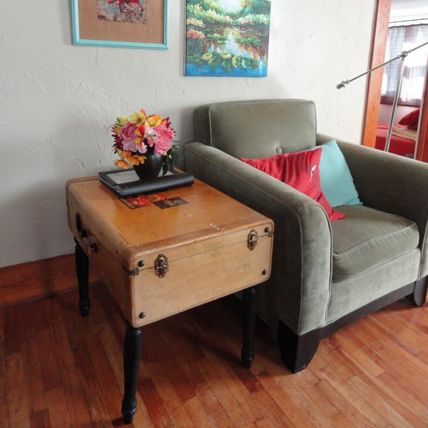 a rustic side table made of a large suitcase placed on black legs is a cool and fresh idea for a retro space and you will get a lot of storage space