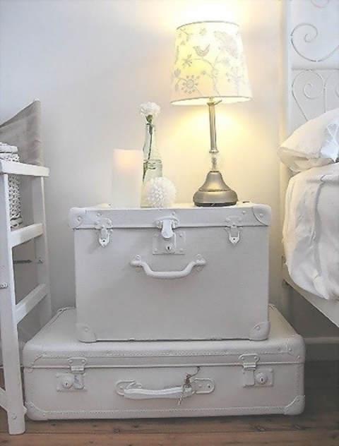 a white shabby chic nightstand composed of vintage suitcases, with a table lamp and some candles and vases is an elegant idea