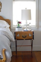 a chic vintage nightstand of a large suticase placed on legs that looks refined and beautiful, a table lamp on it