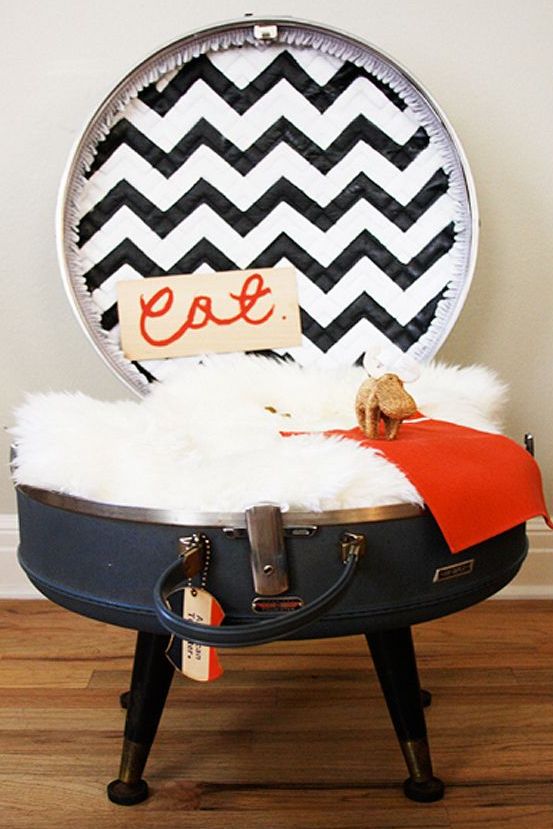 A cat bed made of a large round suitcase placed on legs, with a faux fur cushion, a blanket and a pretty chevron lid is a lovely idea