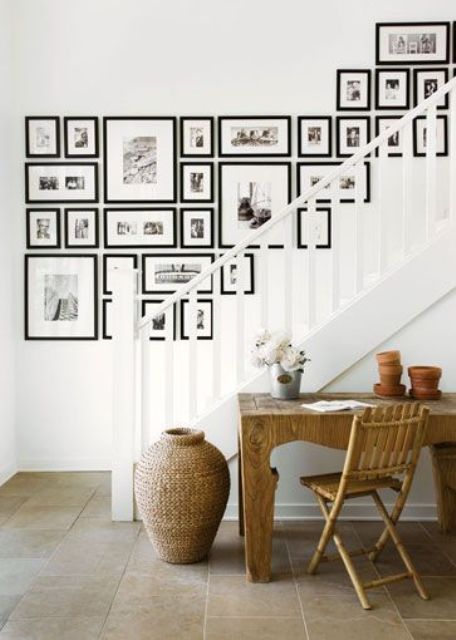 una gran pared de galería sobre la escalera hecha con fotos en blanco y negro en marcos negros es una idea elegante para la decoración del hogar