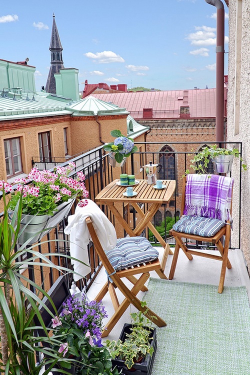 a cheerful summer balcony with bright textiles, potted blooms and greenery and simple wooden folding furniture