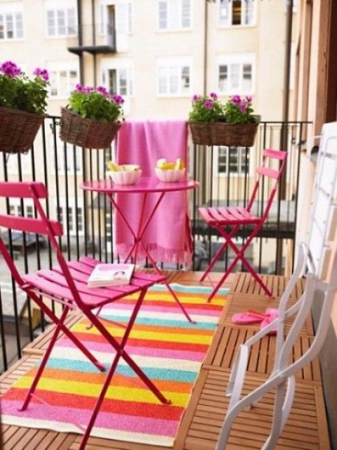 a small and bright summer balcony with a bright rug and blanket, bold pink furniture and potted blooms