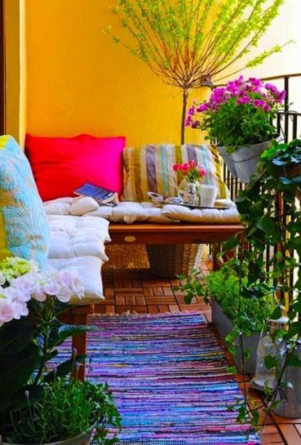 a bright and colorful summer balcony with yellow walls, benches with bright pillows, rugs and potted greenery and blooms