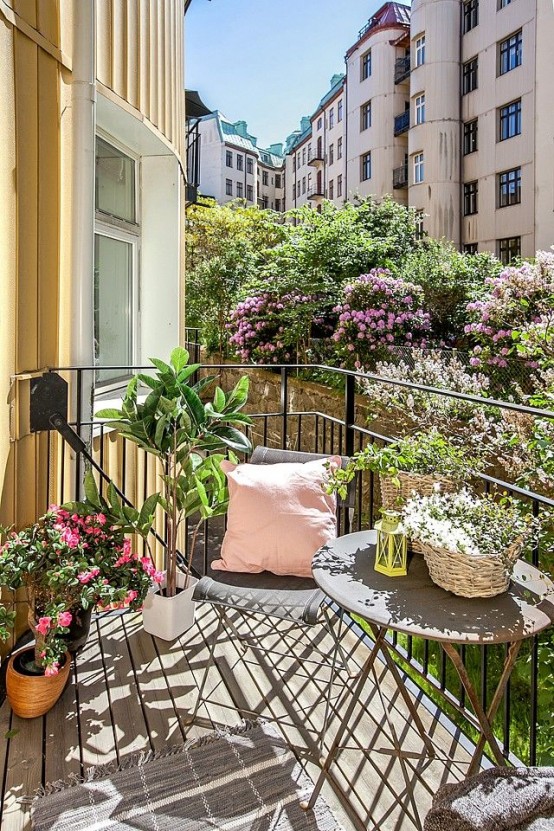 a tiny balcony with lots of potted greenery and blooms and some metal furniture plus some pillows