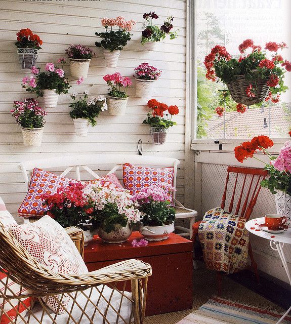 a super bright vintage balcony in white, with lots of red, potted blooms and greenery and bright printed textiles for a bold look