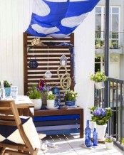 a seaside inspired summer balcony with blue textiles, a painted bench, potted blooms, blue bottles and pillows
