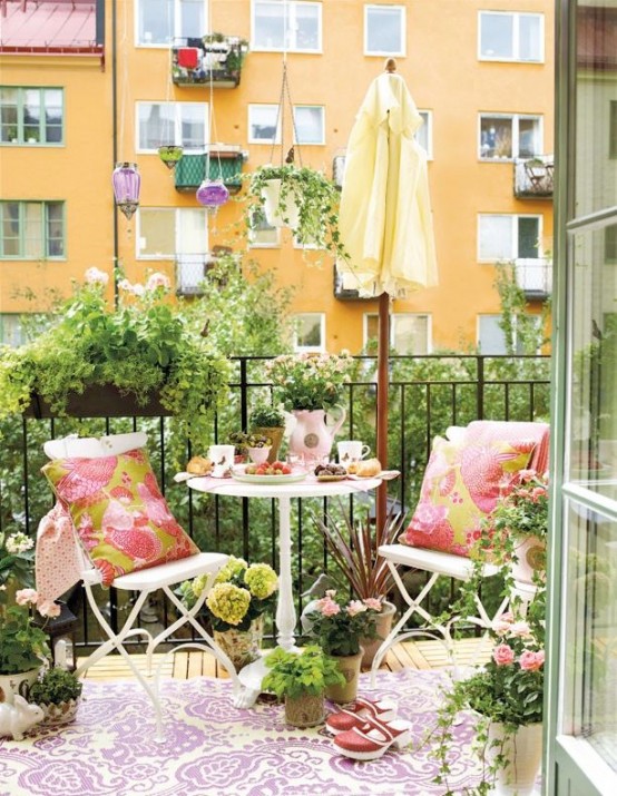 a welcoming summer balcony with simple white metal furniture, colorful printed textiles, potted blooms and greenery