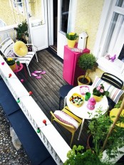 a modern colorful balcony with a wooden floor, metal chairs, colorful textiles and potted greenery