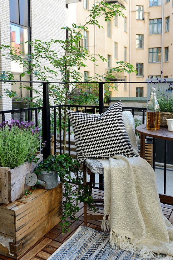 a welcoming summer balcony with wooden crates with greenery and blooms, folding wooden furniture and neutral textiles