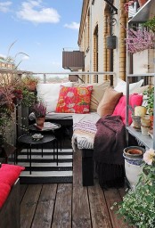 a bright summer balcony with a dark wooden floor, dark wooden furniture, potted greenery and blooms and bright textiles