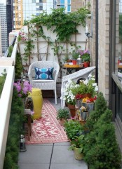 a bright summer balcony with lots of greenery and blooms in pots, with bright rugs and white wicker furniture, bright textiles and accessories
